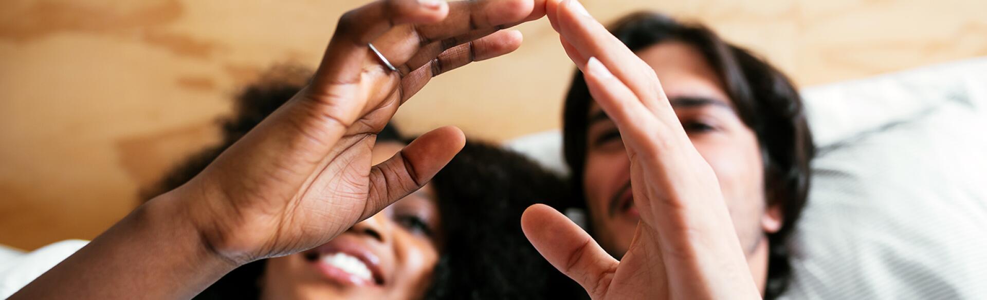 An interracial couple touches fingers while laying in bed.