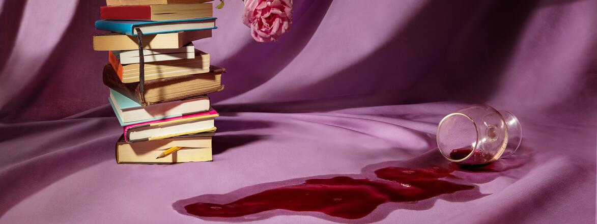 Stack of books with a rose and spilt wine on a violet background