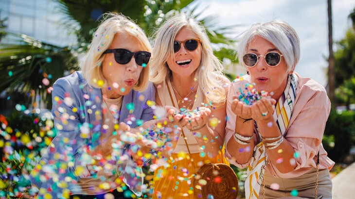 Cheerful senior women celebrating by blowing confetti in the city