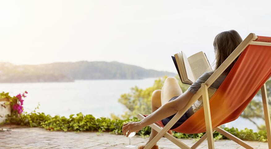Woman reading book while relaxing on deck chair