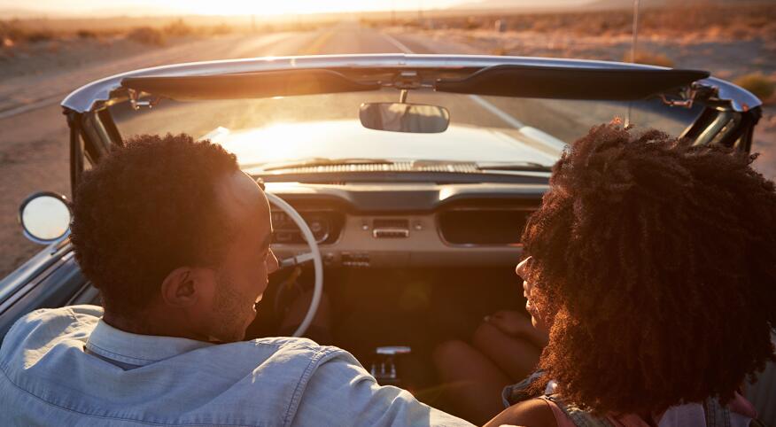 husband and wife in convertible driving into the sunset talking to each other