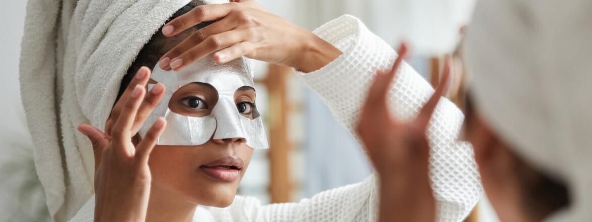 Woman looking in bathroom mirror and putting on beauty face mask
