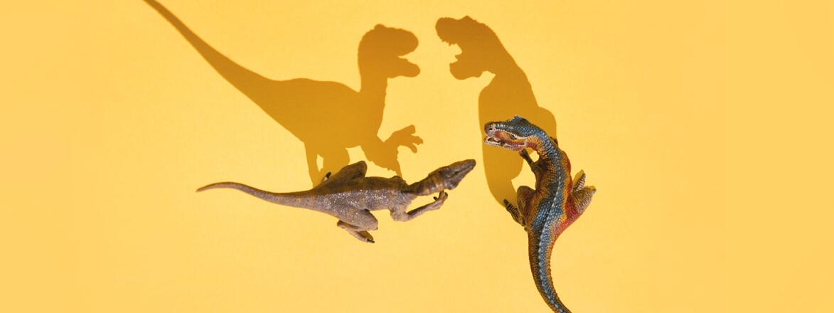 Two toy dinosaurs with mouths open casting long angry shadows