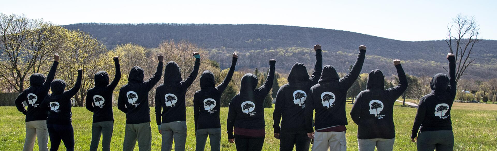 Black women hiking group empowering each other with fists in air outside.