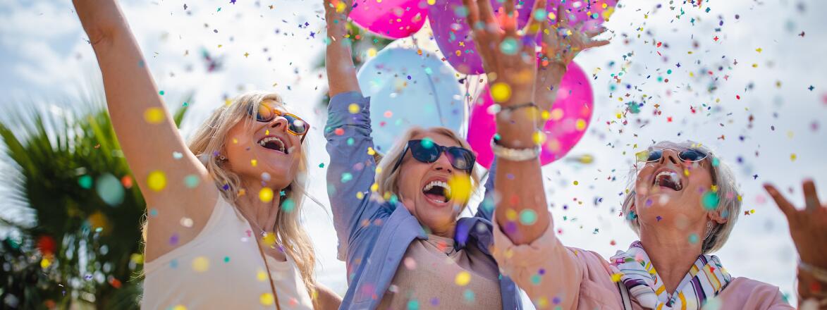 Three women celebrating with colorful confetti and balloons outdoors 