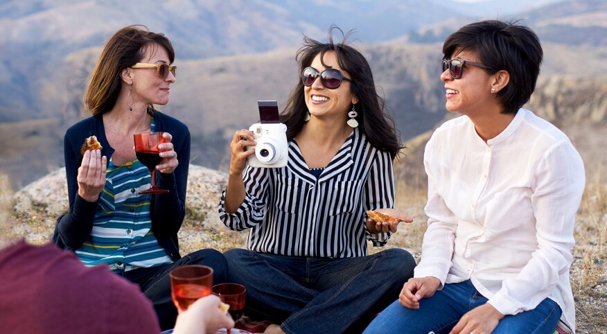 A group of new friends sit outdoors during a picnic in the mountains.