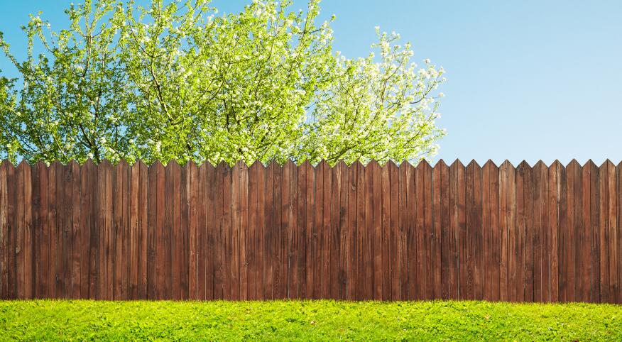 wood stained picket fence in green yard with tree behind it