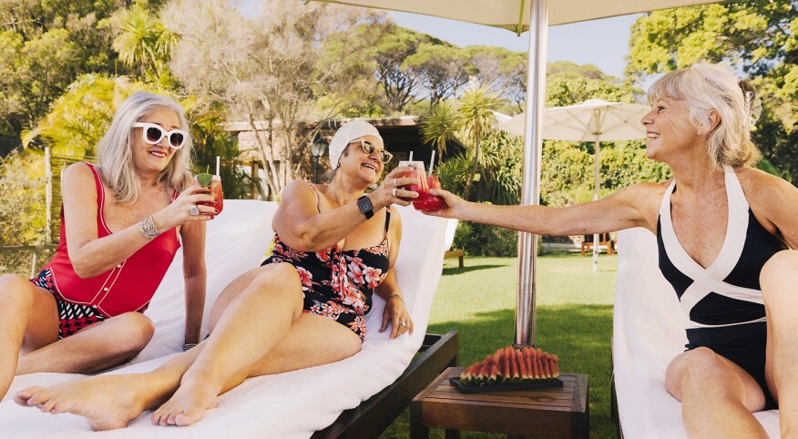 Three mature women toasting by the pool under an umbrella in summer