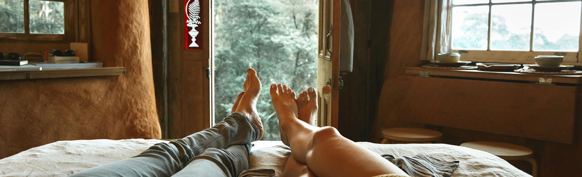 An image of a man and women's legs in bed, where they are lounging together and holding hands.