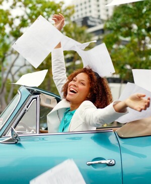 Happy woman in convertible throwing documents into the air