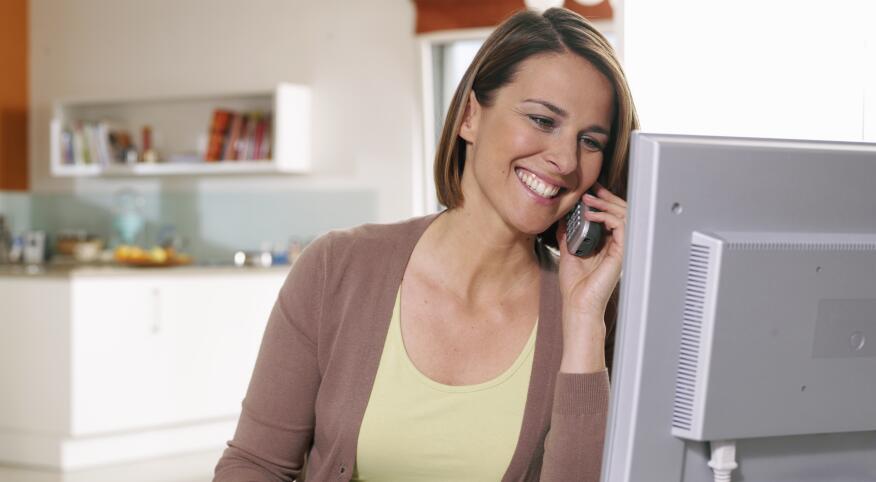 Smiling woman sitting at computer holding telephone