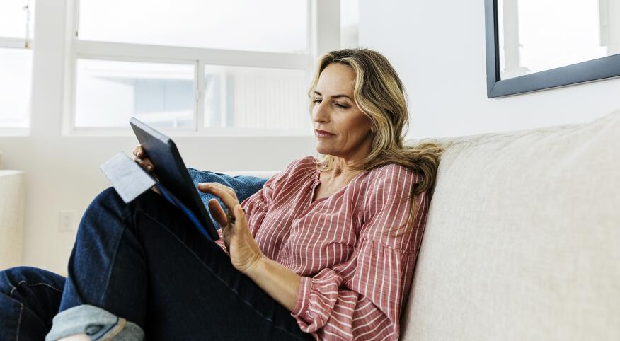 Mature woman using digital tablet while sitting on sofa at home