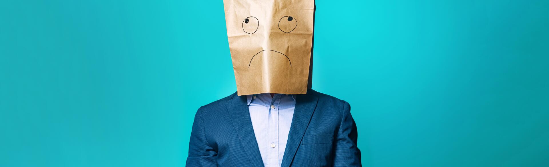 photo of man with paper bag over his head that has sad face drawn on it