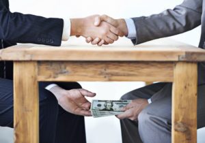 Two men in suits shaking hands while one takes cash