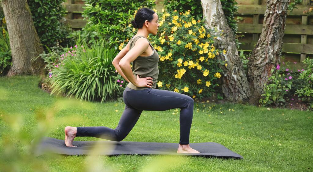 Mature woman doing forward lunges while exercising outdoors.