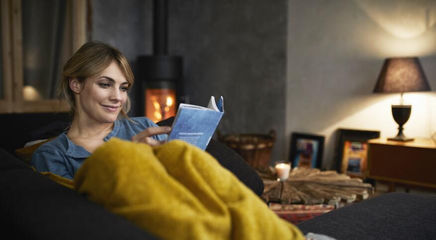 Woman reading book on couch in front of fireplace
