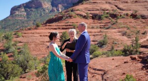 A couple with their officiator standing on red rocks for their private wedding ceremony