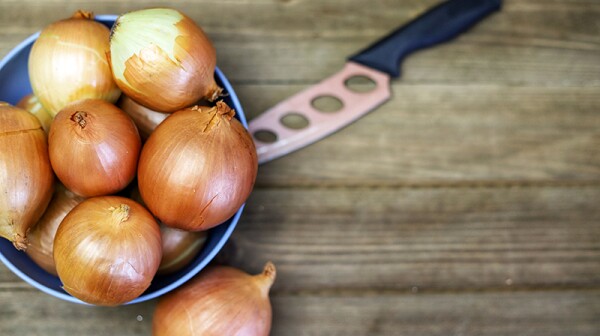 Yellow onions in a blue bowl on a wooden cutting board