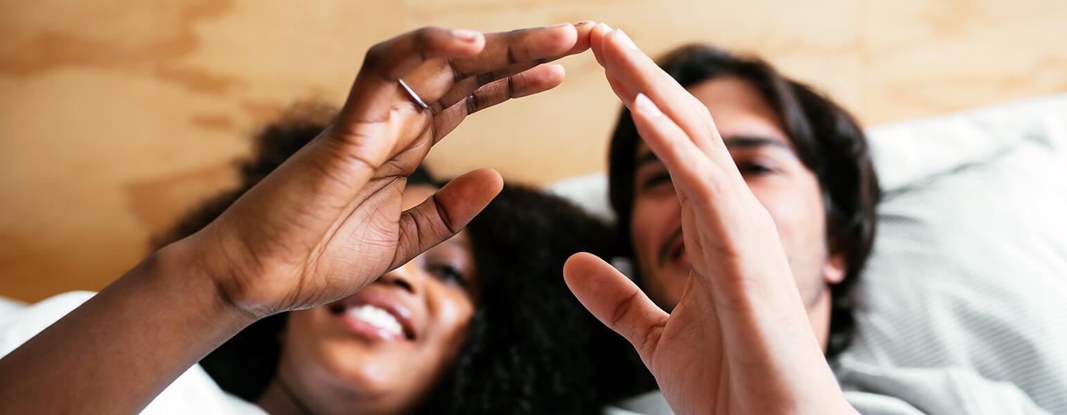 An interracial couple touches fingers while laying in bed.