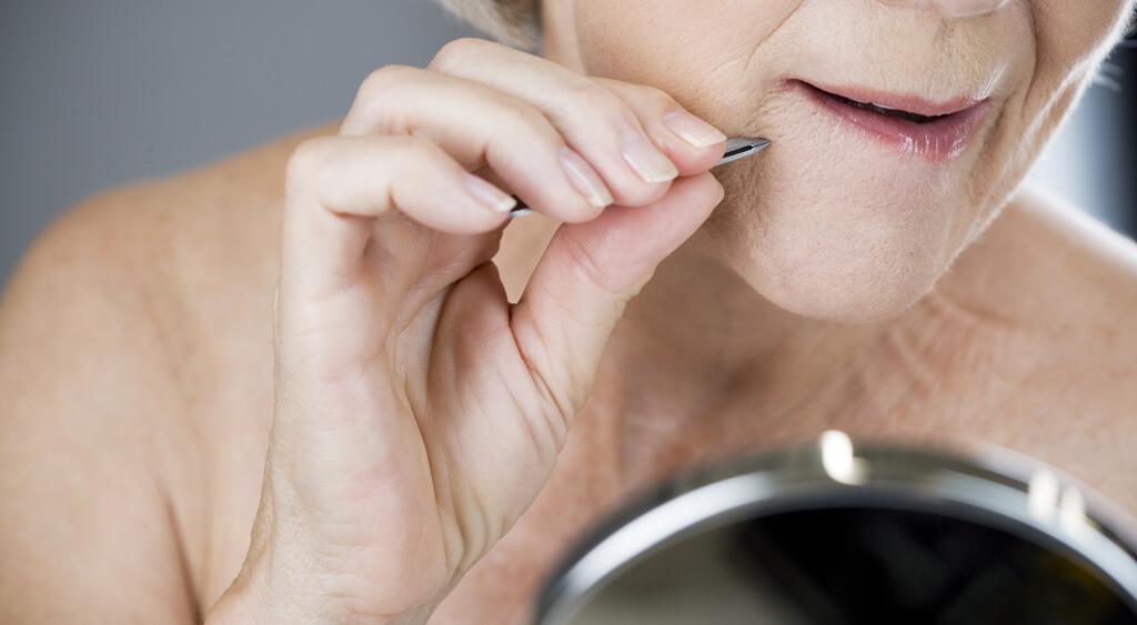 A senior woman plucking hairs from her chin with tweezers