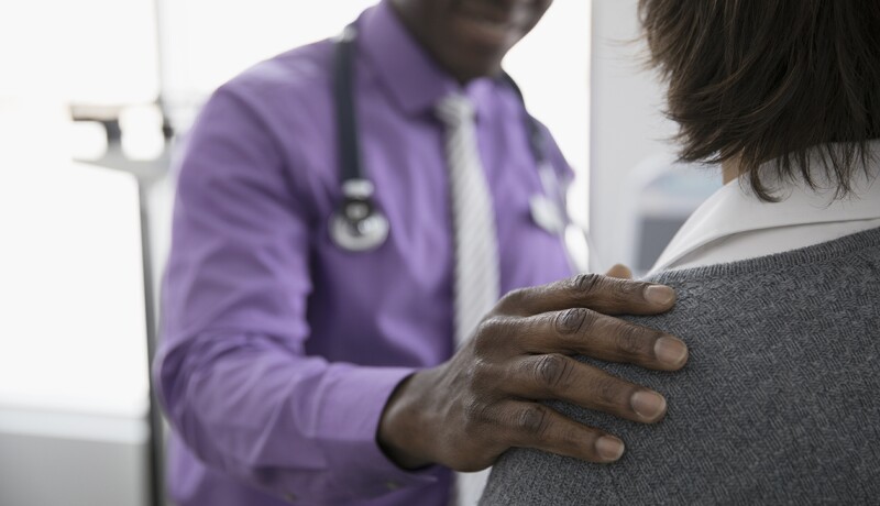 Caring male doctor touching shoulder of female patient in examination room