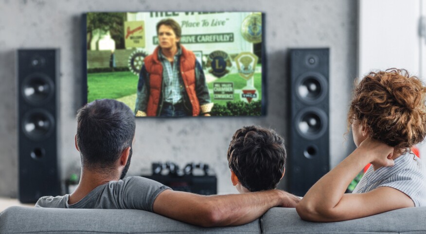 A Mother, Son and Father sitting on a couch together watching a movie in living room.