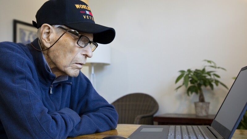 World War Two Veteran wearing cap at home looking at laptop