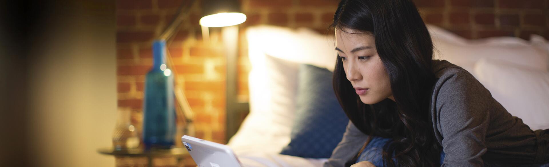 Woman lying on her bed looking at Google on her computer