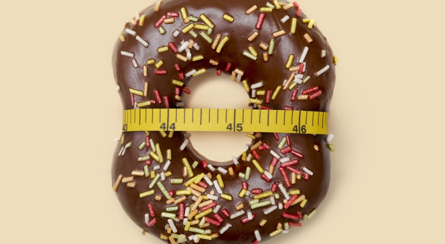 Dieting, conceptual image, a measuring tape tied around a chocolate icing sprinkled doughnut