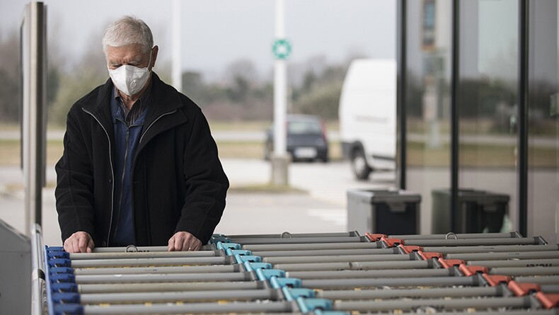 An older man wearing a protective face mask chooses a shopping cart at the supermarket