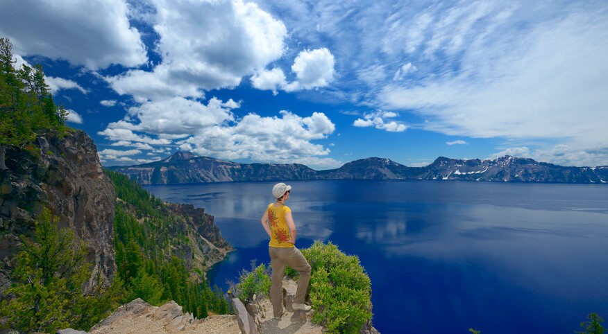Woman with hat standing on rock, overlooking the lake at Crater Lake National Park, Oregon.