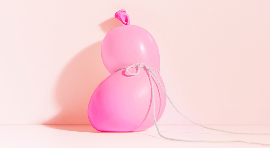 A conceptual still-life witha  pink balloon tied off with a string in the middle 