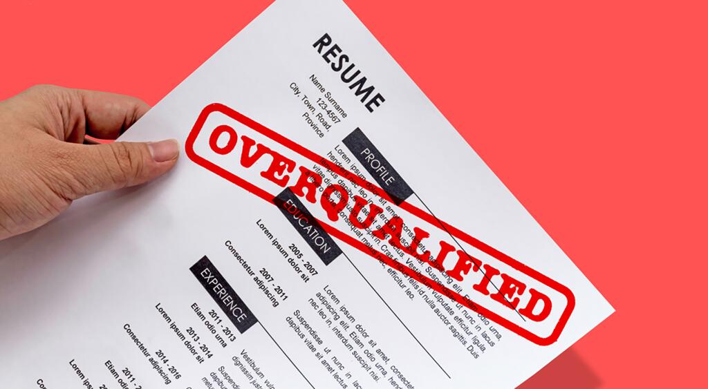 A resume on a printed out piece of paper, with a stamp in red that says OVERQUALIFIED 