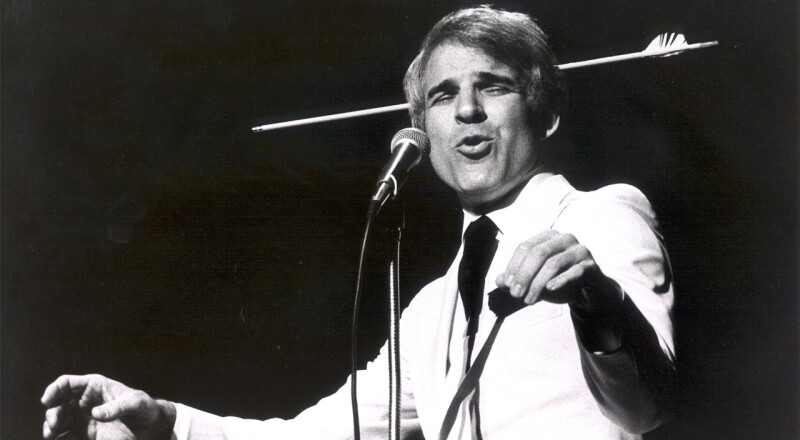 Comedian Steve Martin with a stage prop of a broken arrow on his head