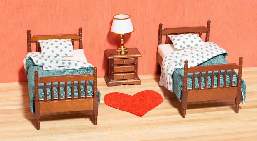 Two twin beds with polka dotted bedding, side by side with side table and red heart rug in the middle