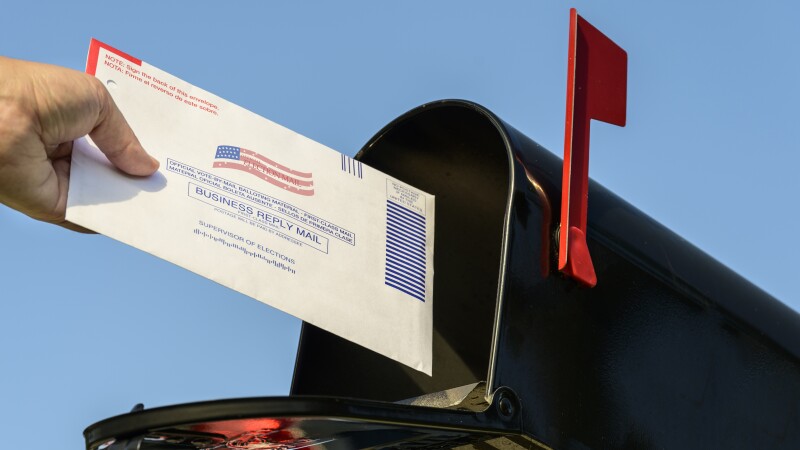 Woman's hand placing a 2020 mail-in election ballot in a rural mailbox