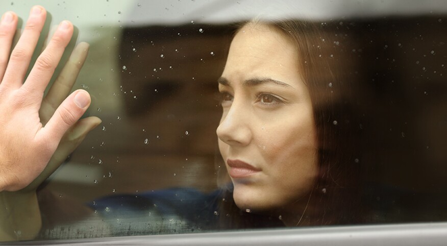 A woman presses her face and hand up against a piece of glass against a parent's hand on the other side.