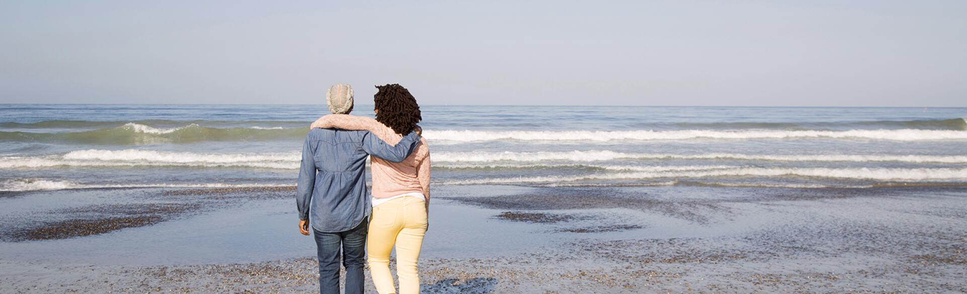 Black women hugging and walking on beach