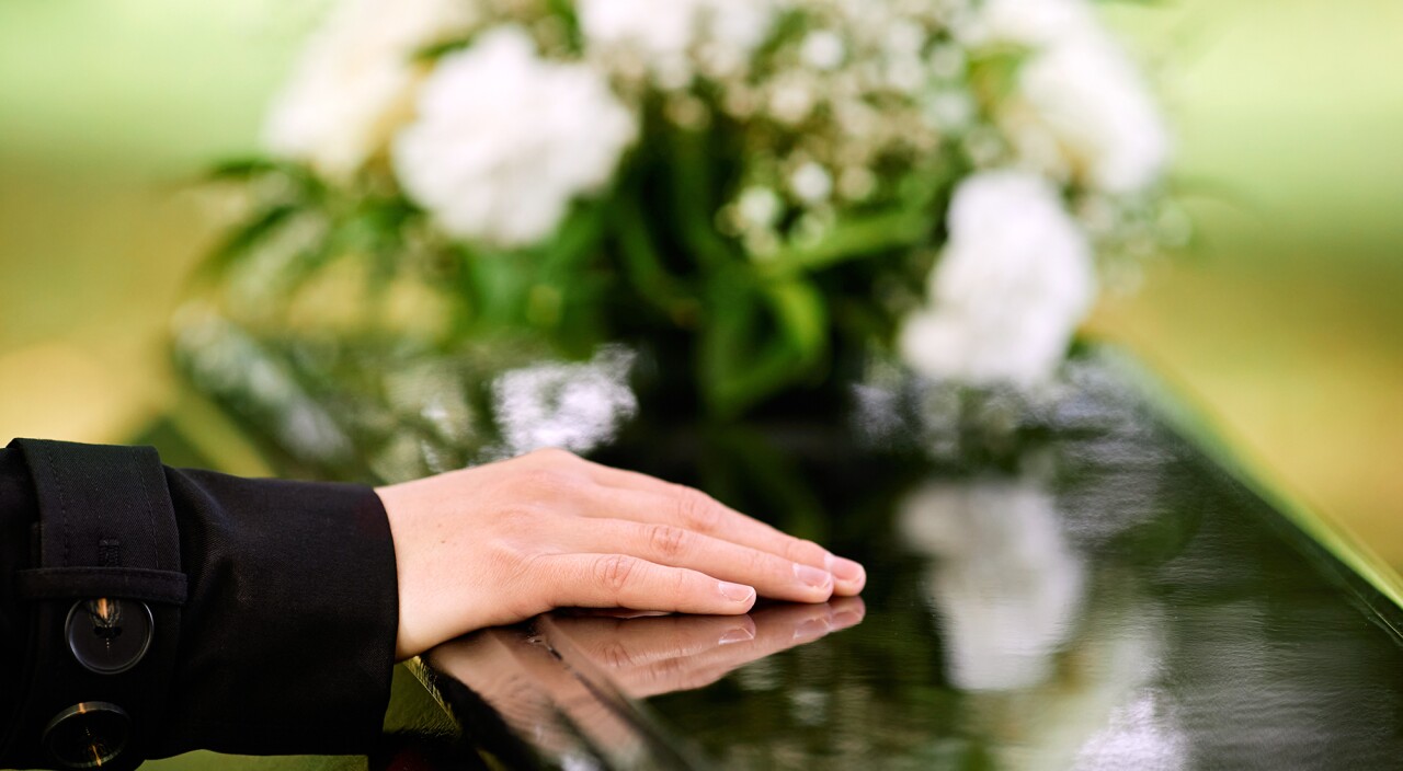 Woman's hand on casket with flowers in the background