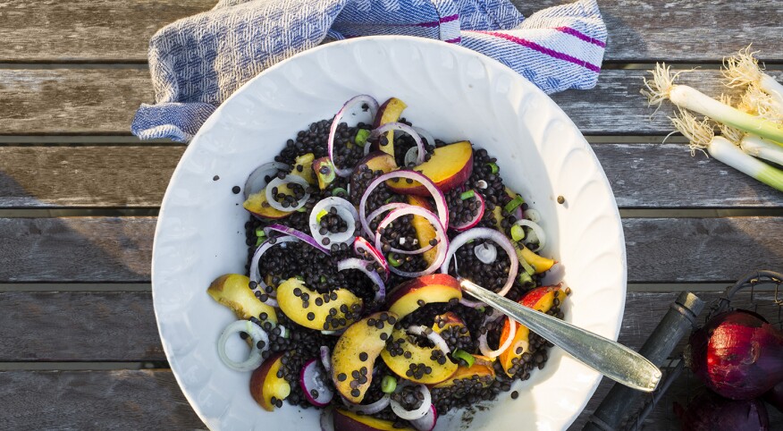 Bowl with lentil and fruit salad on a wooden garden table with kitchen towel