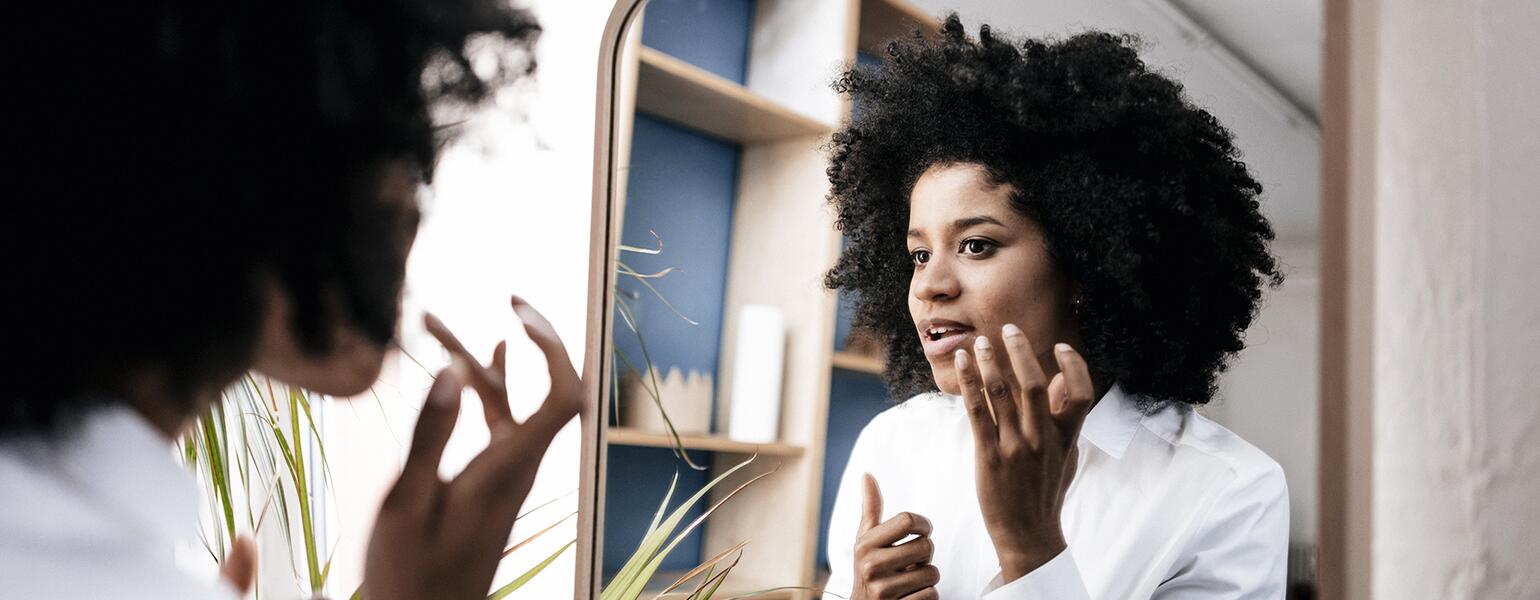 Woman looking in mirror at a dark spot on her face.
