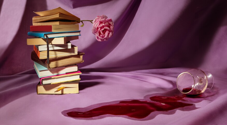 Stack of books with a rose and spilt wine on a violet background