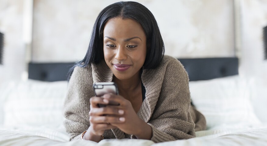 A picture of a woman texting on her cellphone while lying in bed.