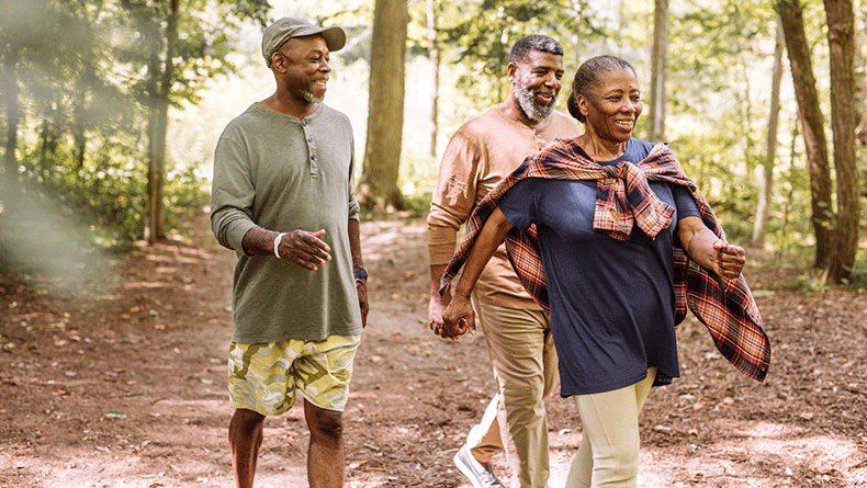 One Black woman and two Black men walk in a forest