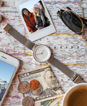 Photo of a U.S. map with miscellaneous travel items on top like a watch, sunglasses, headphones, money, cell phone and polaroid photo.