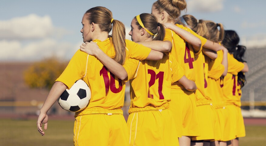 Young girls playing soccer standing on the sidelines arm and arm before the game