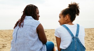 A stepmother sits with her stepdaughter on the beach.