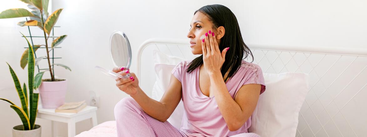 Woman looking in a hand mirror on her bed
