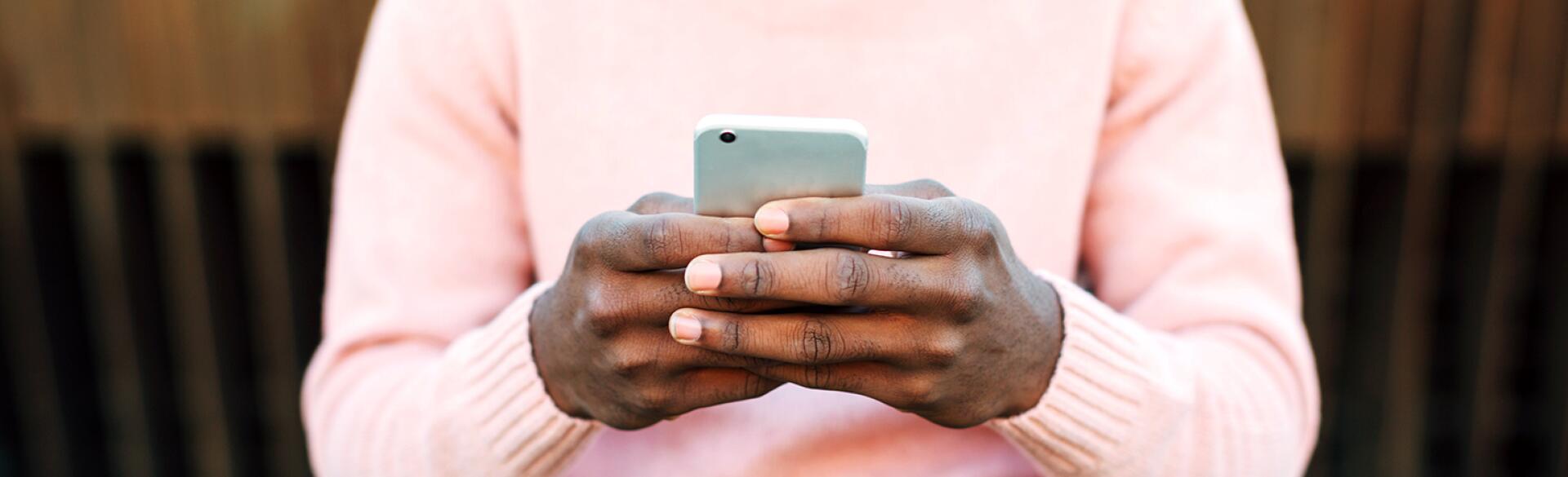 A man holds a cellphone, typing to an unknown person while sitting outside.