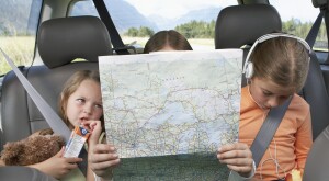 Three girls sitting on rear seat of car on road trip looking at a map